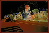 Swamishri on stage with the backdrop depicting different incidents from the life of Bhagwan Swaminarayan 